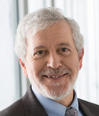 older male with white hair smiling in suit